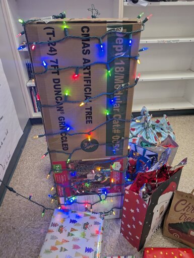 the box of a fake Christmas tree covered in lights with presents under it